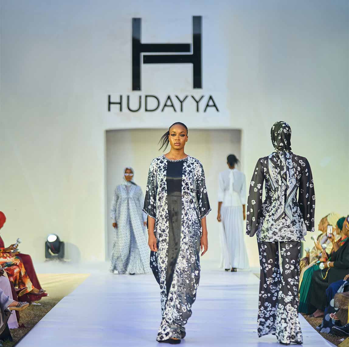 Fashion models walking a runway wearing black and white floral-patterned garments at Hudayya show.