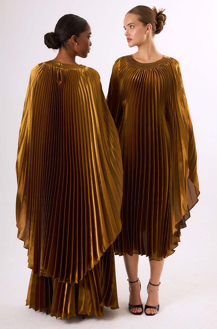 Two women wearing shiny pleated gold midi dresses with long flowing sleeves, one facing forward and the other turned backward.
